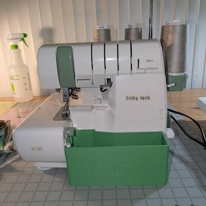 May include: White baby lock serger sewing machine with a green accessory tray. The tray has the text "35th Anniversary Limited Edition". The machine has three spools of thread on top.