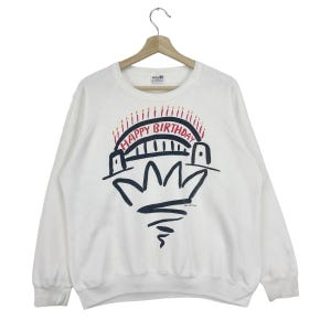 Puede incluir: Sudadera blanca con un gráfico de un puente con velas en la parte superior que dice "Happy Birthday".