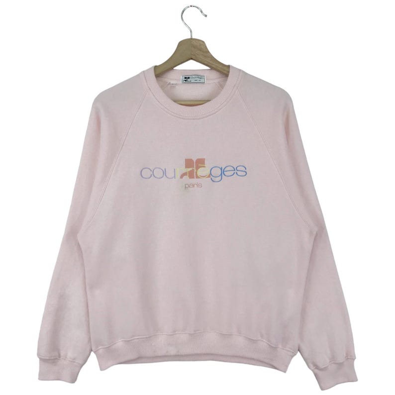 K&ouml;nnte beinhalten: Ein rosa Sweatshirt mit einem bunten "Courr&egrave;ges Paris" Logo auf der Vorderseite.
