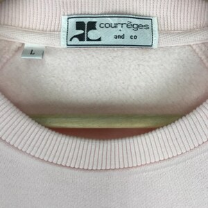 K&ouml;nnte beinhalten: Ein rosa Sweatshirt mit einem wei&szlig;en Etikett mit der Aufschrift "Courr&egrave;ges and co."
