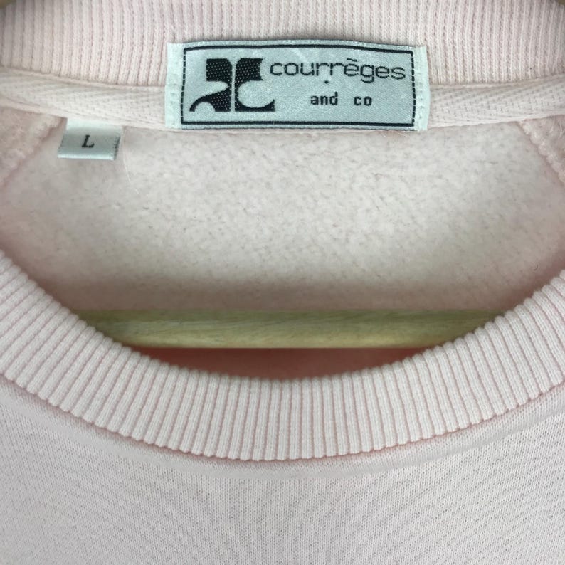 K&ouml;nnte beinhalten: Ein rosa Sweatshirt mit einem wei&szlig;en Etikett mit der Aufschrift "Courr&egrave;ges and co."