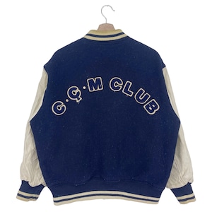 May include: A blue and cream varsity jacket with a cream leather sleeve and a blue embroidered "C.Q.M CLUB" on the back.