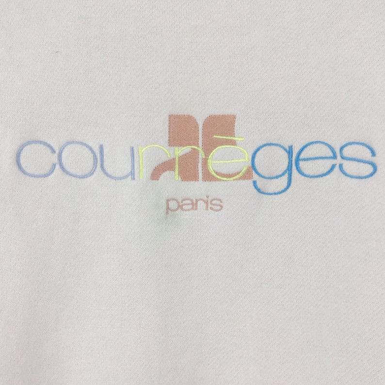 K&ouml;nnte beinhalten: Wei&szlig;er Pullover mit einem mehrfarbigen gestickten Logo, auf dem "Courr&egrave;ges Paris" steht.