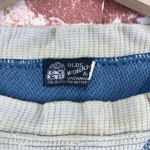 May include: A black and white label with the text "Olds Workmanship & Unchang The Best of the Better" on a blue and white striped fabric.