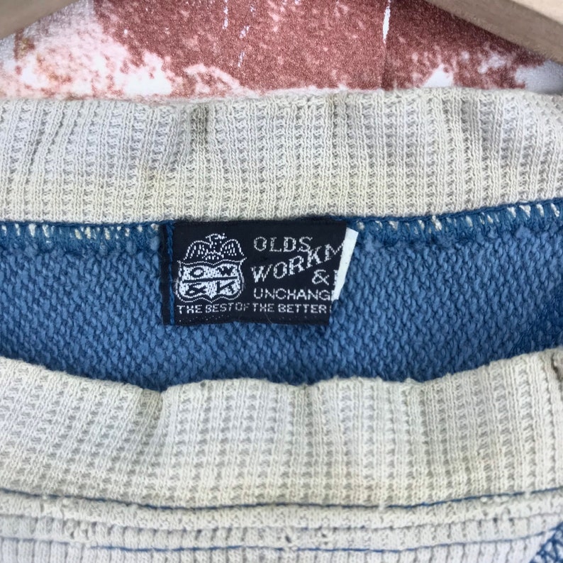 May include: A black and white label with the text "Olds Workmanship & Unchang The Best of the Better" on a blue and white striped fabric.