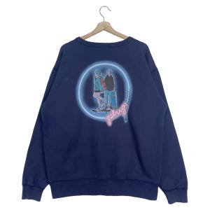 May include: A navy blue sweatshirt with a graphic of two people skateboarding in a neon circle with the word "plug" written in neon letters.