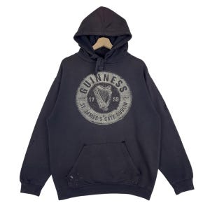 May include: Dark grey hooded sweatshirt with a front pocket and drawstring. The front displays a distressed circular graphic with "GUINNESS" and a harp, plus "ST. JAMES'S GATE DUBLIN".