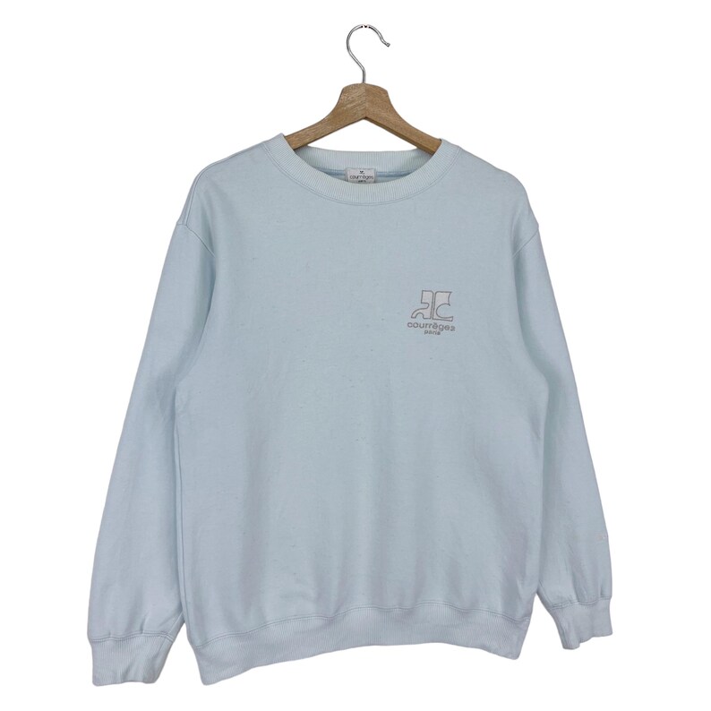 Puede incluir: Una sudadera de color azul claro con un logotipo blanco que dice "Courreges Paris" y un gr&aacute;fico de una "C" estilizada.