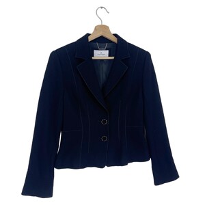 K&ouml;nnte beinhalten: Ein marineblauer Blazer mit einem einzigen Knopfverschluss und zwei Zierkn&ouml;pfen. Der Blazer hat einen Schalkragen und lange &Auml;rmel.
