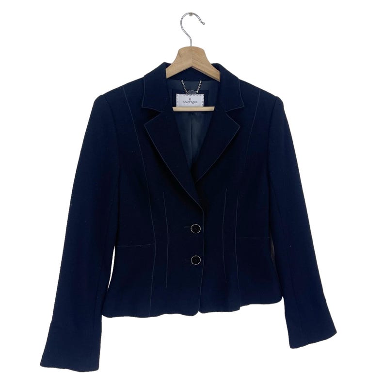 K&ouml;nnte beinhalten: Ein marineblauer Blazer mit einem einzigen Knopfverschluss und zwei Zierkn&ouml;pfen. Der Blazer hat einen Schalkragen und lange &Auml;rmel.