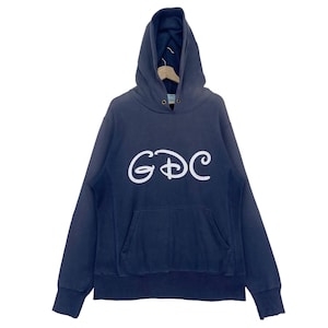 Puede incluir: Una sudadera con capucha azul marino con un logotipo GDC blanco en la parte delantera. El logotipo está estilizado para parecerse al logotipo de Disney.