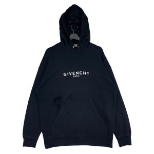 Pode incluir: Moletom preto com capuz com o texto branco "GIVENCHY PARIS" no peito. O moletom tem um bolso frontal e uma área danificada perto do bolso. O moletom com capuz está pendurado em um cabide preto.