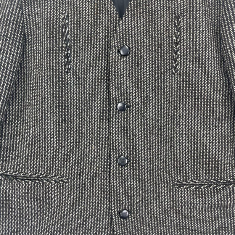 May include: A black and white striped blazer with a v-neck and five black buttons. The blazer has two pockets on the bottom and decorative stitching on the front.