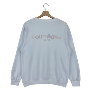 Puede incluir: Una sudadera azul claro con un logotipo "Courr&egrave;ges Paris" multicolor en la espalda.