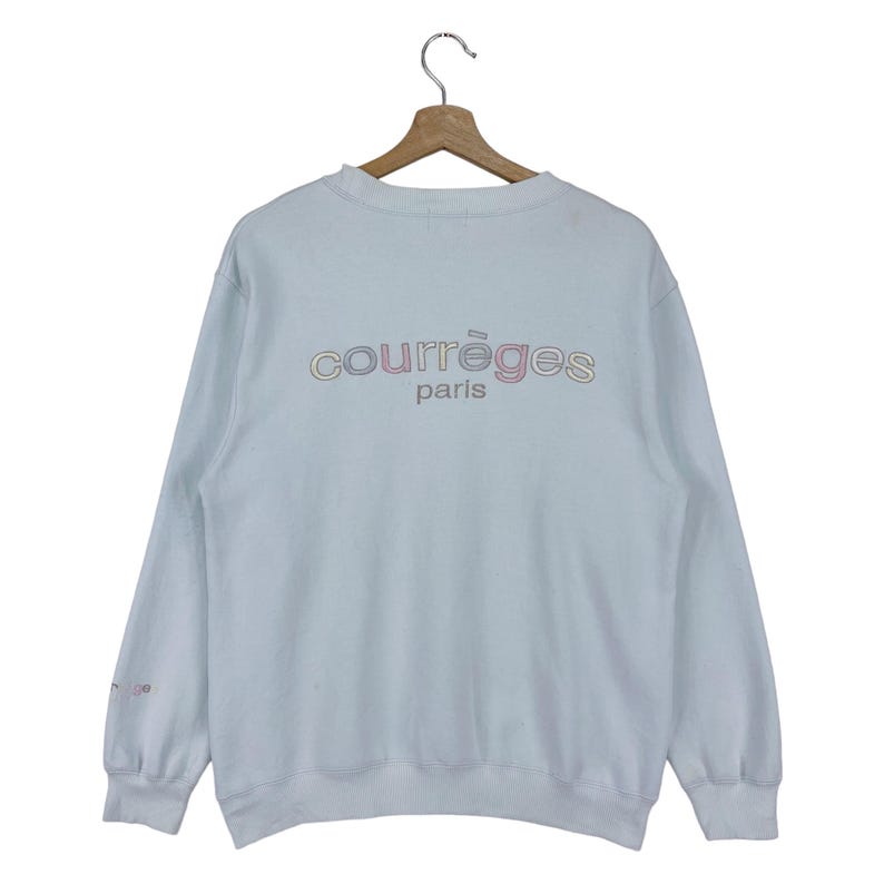 Puede incluir: Una sudadera azul claro con un logotipo "Courr&egrave;ges Paris" multicolor en la espalda.