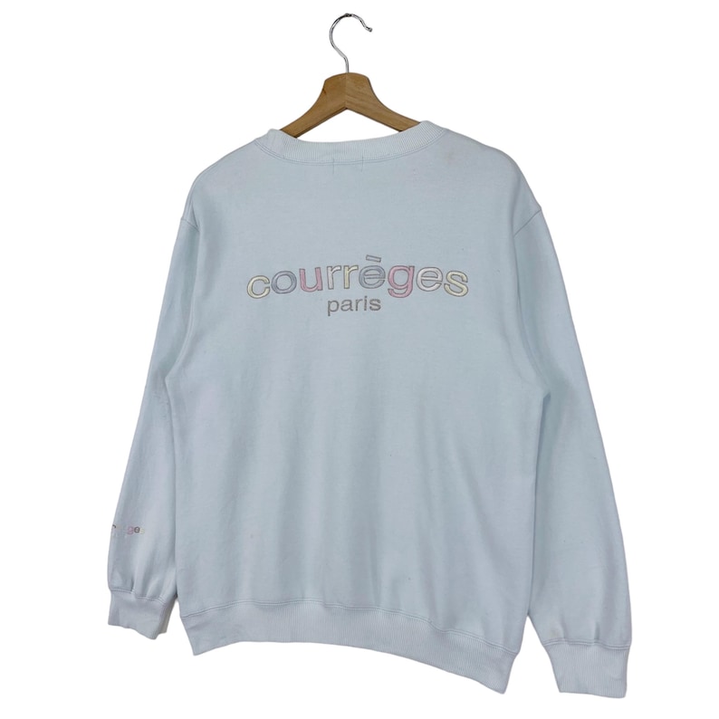 Puede incluir: Una sudadera azul claro con un logotipo "Courr&egrave;ges Paris" multicolor en la espalda.