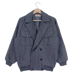 以下が含まれることがあります： 内側に「Wrangler Calls」のラベルが付いた、グレーのダブルブレストウールジャケット。大きなフラップポケットが2つ付いている。