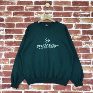 May include: A dark green sweatshirt with a white Dunlop Motor Sport logo on the front.