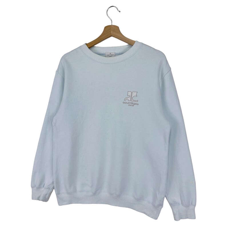 Puede incluir: Una sudadera azul claro con un logotipo rosa y blanco que dice "Courr&egrave;ges".