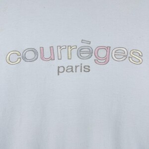 Puede incluir: Una camiseta azul claro con el texto "courr&egrave;ges paris" en bordado multicolor.