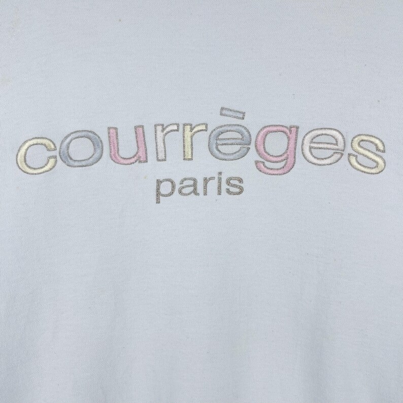 Puede incluir: Una camiseta azul claro con el texto "courr&egrave;ges paris" en bordado multicolor.