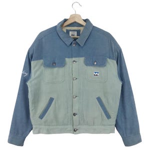 Puede incluir: Una chaqueta de pana azul y verde claro con forro de sherpa. La chaqueta tiene cierre de botones, dos bolsillos de solapa en la parte delantera y un parche de logotipo en el pecho derecho. El texto "Billabong" está bordado en la manga izquierda.