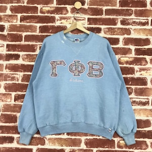 Peut inclure: Sweat-shirt bleu clair avec un motif de lettres grecques à motifs floraux qui dit "ΓΦΒ Alabama".