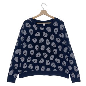 Puede incluir: Una sudadera negra de manga larga con un estampado de calaveras blancas. La sudadera tiene cuello redondo y un corte holgado.