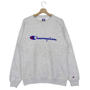 May include: A gray Champion sweatshirt with a blue and red logo on the front. The logo says "Champion" in a cursive font.