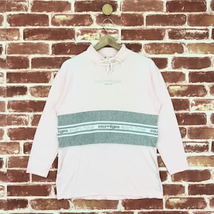 Op de afbeelding: Een lichtroze sweatshirt met lange mouwen en een grijze horizontale streep over de borst. De grijze streep heeft de tekst "courr&egrave;ges sport futur" in het wit. Het woord "courr&egrave;ges paris" staat boven de streep. De sweatshirt heeft een hoge halslijn met een trekkoord.