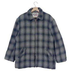 Op de afbeelding: Een grijs en zwart geruit jack met rits en het label "Rugby" op de linkerborst.