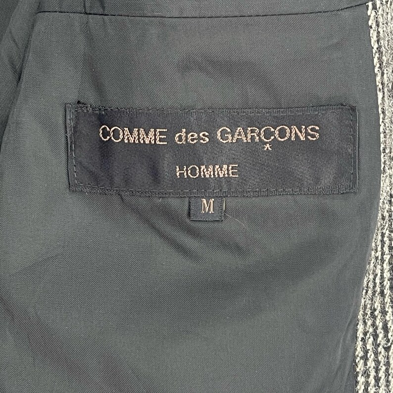 May include: Black label with white text reading "COMME des GAR&Ccedil;ONS" and "HOMME" with a size "M" label below.