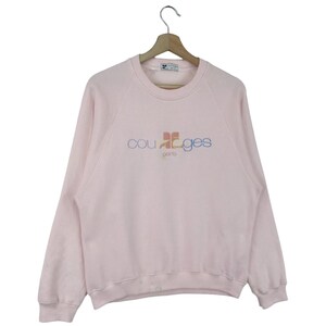 K&ouml;nnte beinhalten: Ein rosa Sweatshirt mit einem bunten "courages paris" Logo auf der Vorderseite.