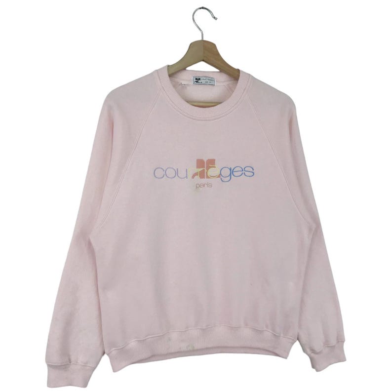 K&ouml;nnte beinhalten: Ein rosa Sweatshirt mit einem bunten "courages paris" Logo auf der Vorderseite.