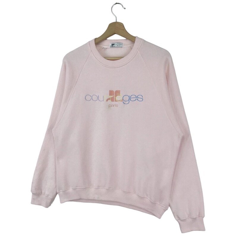 K&ouml;nnte beinhalten: Ein rosa Sweatshirt mit einem bunten "Courr&egrave;ges Paris" Logo auf der Vorderseite.