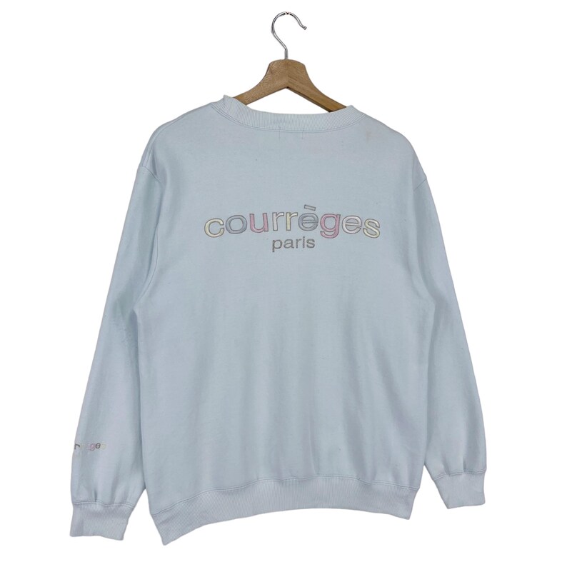 Puede incluir: Una sudadera azul claro con un logotipo "Courr&egrave;ges Paris" multicolor en la espalda.
