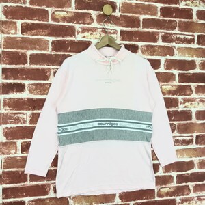 Op de afbeelding: Een lichtroze sweatshirt met lange mouwen en een grijze horizontale streep over de borst. De grijze streep heeft de merknaam "courr&egrave;ges" in het wit. De sweatshirt heeft een hoge halslijn met een trekkoord.