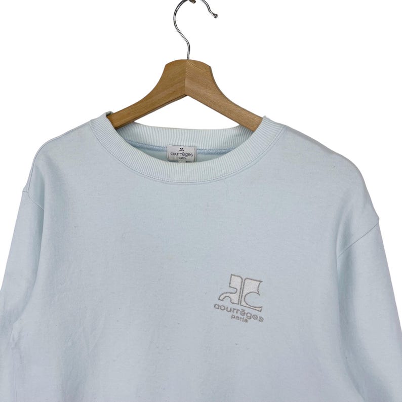 Puede incluir: Una sudadera azul claro con un logotipo bordado en blanco que dice "Courr&egrave;ges Paris".