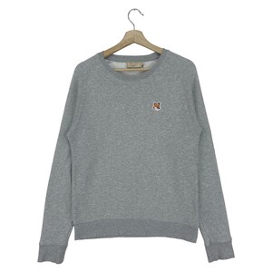 May include: A gray sweatshirt with a small fox logo on the left chest. The sweatshirt has a crew neck and long sleeves.