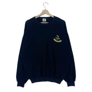 May include: Black long-sleeve sweatshirt with a Puma logo and a graphic of an apple with the text "Puma is the new black" on the front.
