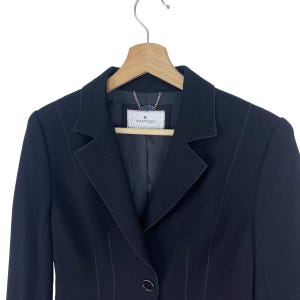 K&ouml;nnte beinhalten: Ein schwarzer Blazer mit einem einzigen Knopfverschluss und einem Etikett mit der Aufschrift "Courr&egrave;ges" auf der Innenseite.