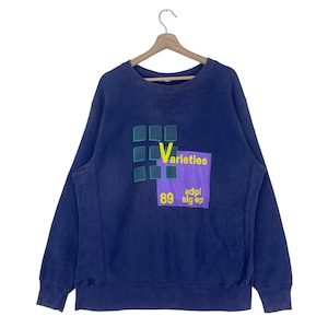 May include: A navy blue sweatshirt with a colorful graphic design featuring the word "Varieties" in yellow letters, a purple rectangle with the text "adpl slg ep" in yellow letters, and a grid of squares in green and blue. The number "89" is printed in yellow below the purple rectangle.
