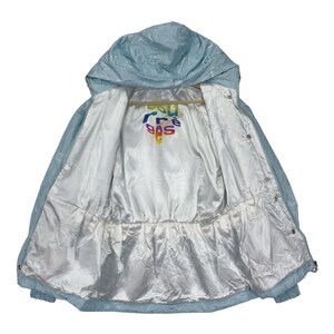 K&ouml;nnte beinhalten: Eine hellblaue Kapuzenjacke mit wei&szlig;em Futter. Das Futter hat ein regenbogenfarbenes "Sea Free" Logo.