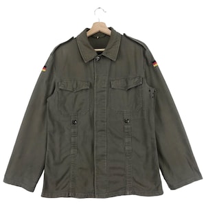 May include: A green military-style jacket with a button-up front and two large flap pockets. The jacket has a German flag patch on the sleeve.