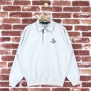 May include: A white long-sleeve polo shirt with a black collar and button placket. The shirt features an embroidered logo that says "Jaguar Club" with a stylized car image.