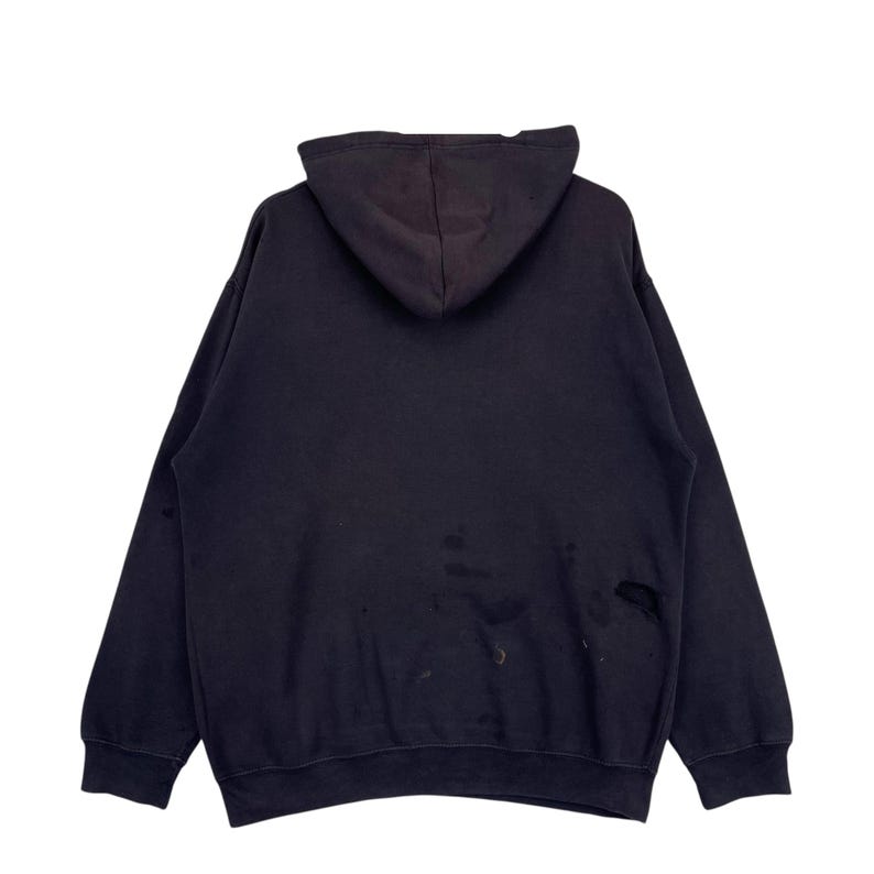 May include: A black hooded sweatshirt, seen from the rear. The garment shows signs of wear, with visible marks and small holes. The material looks to be soft and comfortable.
