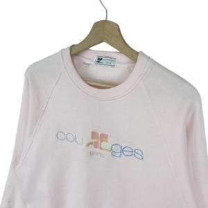 K&ouml;nnte beinhalten: Ein rosa Sweatshirt mit einem mehrfarbigen "Courr&egrave;ges Paris" Logo auf der Vorderseite.
