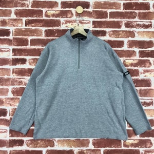 May include: A gray long-sleeve pullover with a half-zip closure and a small logo patch on the sleeve.