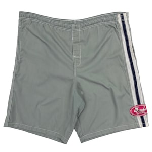 Puede incluir: Bañador gris con una raya blanca y azul marino a lo largo del lateral. El bañador tiene un logotipo rosa que dice "Mambo Surf Life" en la pierna derecha.