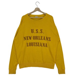May include: A yellow sweatshirt with a brown print that reads "U.S.S. NEW ORLEANS LOUISIANA"